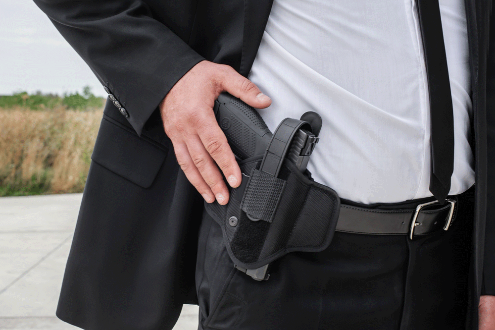 Close-up of an armed security guard in a suit, reaching for a holstered firearm, representing professional armed security services.